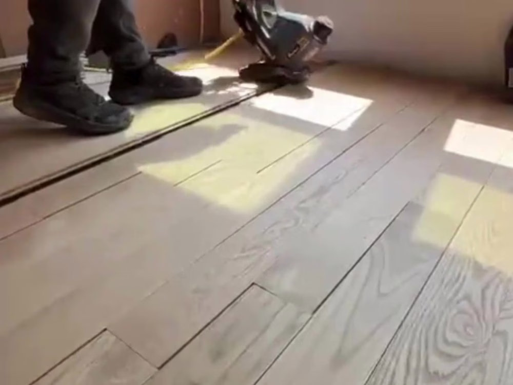 Close-up of unfinished flooring installation showing a worker fitting 4” white oak planks with a floor nailer during a hardwood installation project.