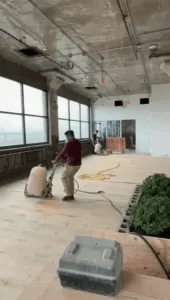 Floor sanding and finishing worker operating large sanding machine in industrial-style room.