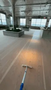 Floor sanding and finishing using mop tool to spread treatment on large surface.