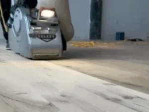 Worker performing hardwood floor sanding with Galaxy machine.