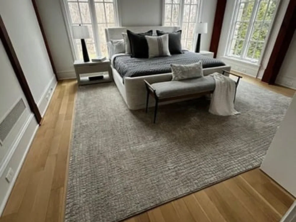 Bright bedroom showcasing wood floor restoration with tall windows and layered textures.