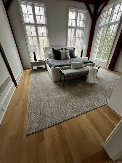 Bedroom with wood floor restoration featuring a large neutral rug and modern décor.