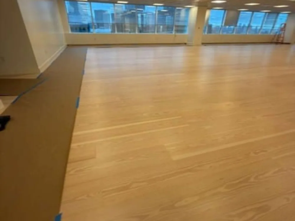 Commercial hardwood floor installation in open office area with large windows
