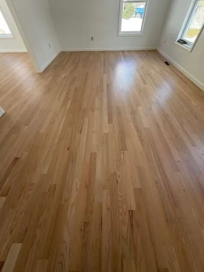 Corner view of a room displaying the results of a natural wood floor restoration on light oak planks.