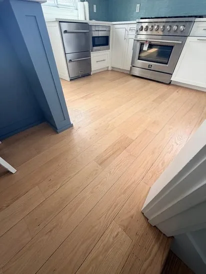 Modern kitchen area transitioning into a space with natural satin hardwood floors.